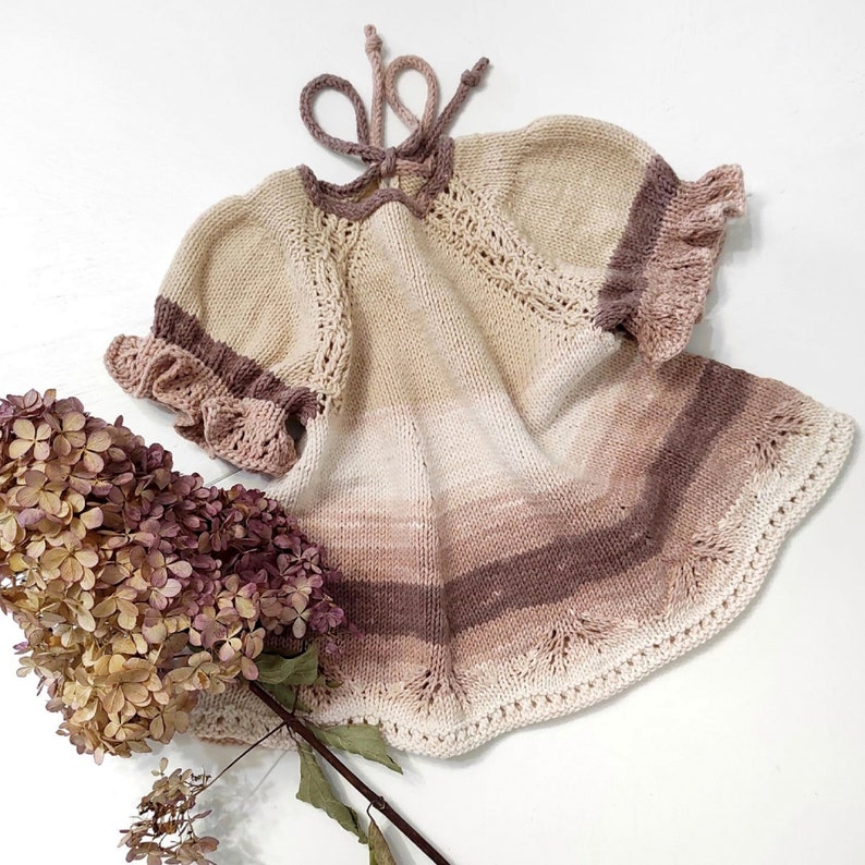 May include: A knitted baby dress with a gradient of beige, pink, and brown. The dress has a ruffled neckline and sleeves.