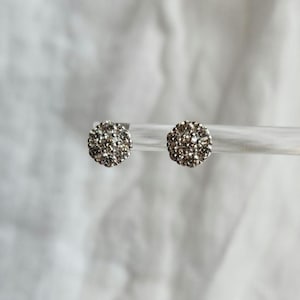 May include: A pair of silver stud earrings with a cluster of small, clear diamonds set in a round shape.