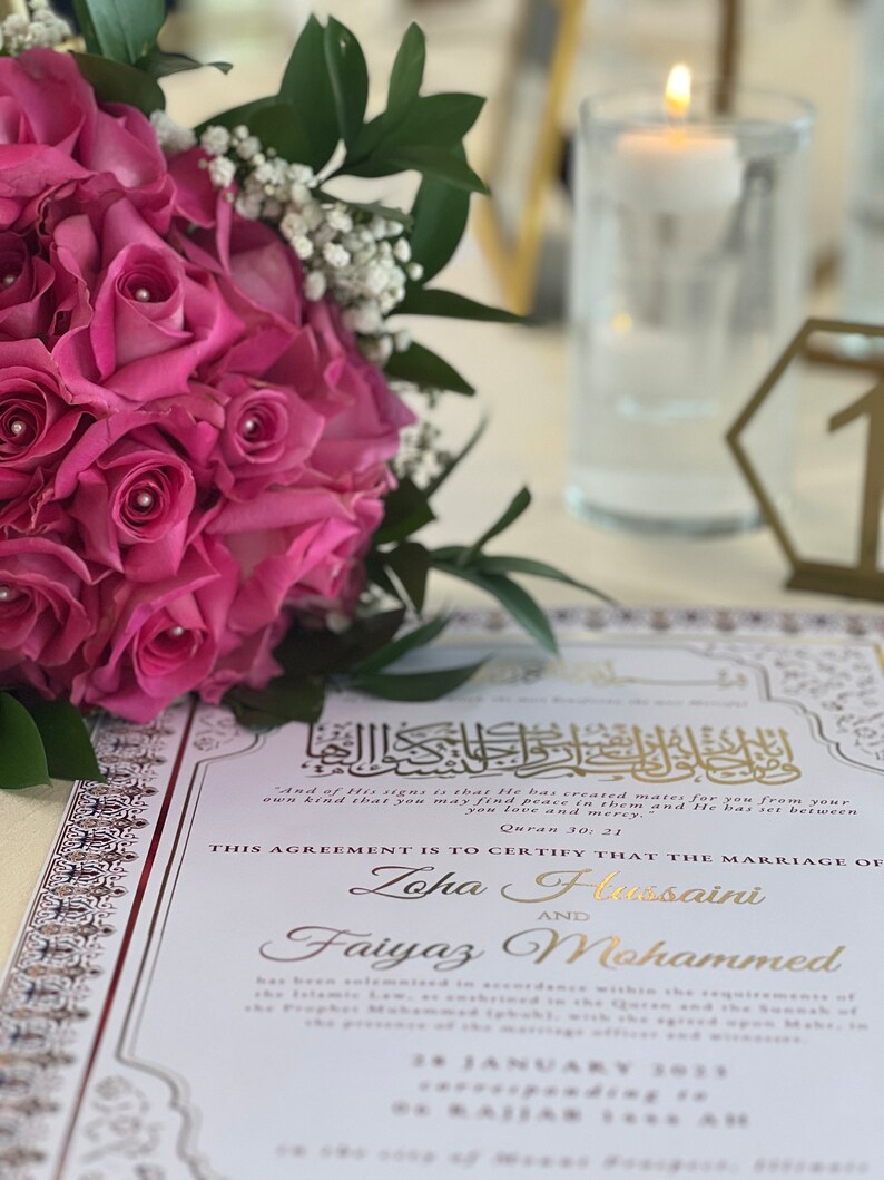 May include: A white wedding ceremony card with gold accents and Arabic calligraphy. The card states "This agreement is to certify that the marriage of Zoha Hussaini and Faiyaz Mohammed." The date of the ceremony is January 28, 2023.