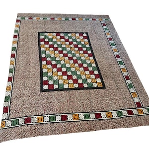 May include: A rectangular brown rug with a central checkered pattern in red, green, yellow, and white. The rug has a border with repeating geometric designs in red, green, yellow, and white.