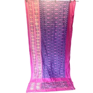 Pode incluir: Um tecido vibrante com um padrão geométrico em tons de roxo, rosa e branco. O tecido é drapeado, mostrando um design detalhado. O tecido tem uma borda rosa e é provavelmente um item decorativo.