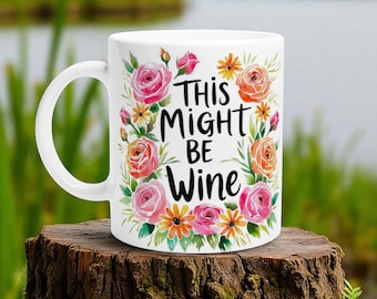May include: White ceramic mug with the text "This Might Be Wine" surrounded by a floral wreath of pink and orange roses, yellow daisies, and green leaves. The mug has a white handle.