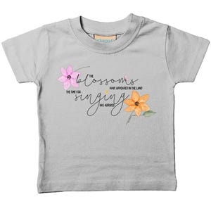 May include: A light grey t-shirt with a floral design and the text "The blossoms have appeared in the land, the time for singing has arrived."
