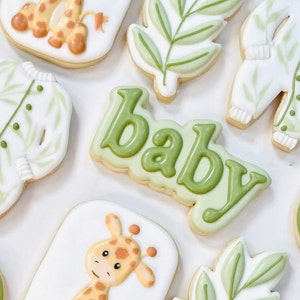 May include: A set of nine decorated sugar cookies with a baby theme. The cookies are decorated with green leaves, a giraffe, and the word "baby".
