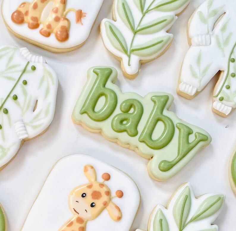 May include: A set of nine decorated sugar cookies with a baby theme. The cookies are decorated with green leaves, a giraffe, and the word "baby".