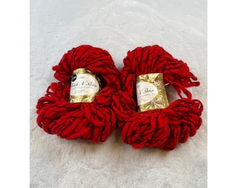 May include: Two skeins of red knitting yarn. Each skein has a gold label that reads "Thick 'N Thin" and "Knitting Yarn". The yarn is a thick, textured material, perfect for various knitting projects.