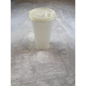 Può includere: Un contenitore per bevande in plastica traslucida con un coperchio colorato chiaro e un piccolo beccuccio rotondo. Il contenitore è cilindrico con una base leggermente svasata. Il coperchio ha una piccola apertura circolare per versare.