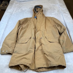 May include: A tan hooded jacket with a drawstring waist and two front pockets. The jacket has a blue lining in the hood and is buttoned at the cuffs. The jacket is laid flat on a white surface.