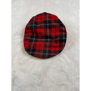 May include: A red and black plaid newsboy cap. The cap features a classic plaid pattern in red and black, with thin white and tan lines. The cap is made of a soft material and is a stylish accessory.