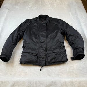 May include: Black motorcycle jacket with a stand-up collar, two front pockets, and adjustable cuffs. The jacket has a zipper closure and a belt at the waist. The jacket is made of a durable, water-resistant material.