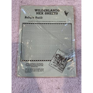 May include: A package of Wilderlands Hex Sheets by Judges Guild, featuring a large grid of small hexagons on a light gray background. The text includes 'WILDERLANDS HEX SHEETS', 'FOUR MAPS 17x22', and details about the campaign maps and hex numbering.