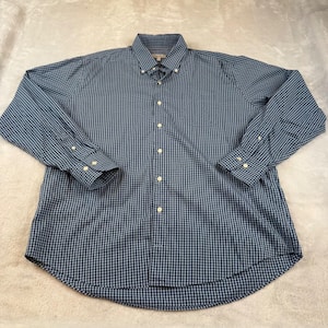 Könnte beinhalten: Ein langärmliges Hemd mit blau-weißem Karomuster. Es hat einen Button-Down-Kragen und geknöpfte Manschetten. Der Stoff scheint leicht zu sein, möglicherweise Baumwolle oder eine Mischung.