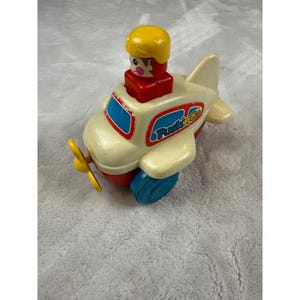 May include: A vintage toy airplane in cream, red, and blue. The toy features a yellow propeller, blue wheels, and a small pilot figure. The plane has the words "Push 'n Go" printed on the side.