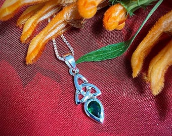 May include: A silver Celtic knot pendant necklace with a green gemstone. The necklace is on a red fabric background.