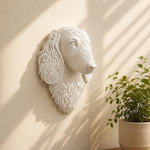 May include: A white wall-mounted sculpture of a dog head featuring intricate, embossed floral and swirling patterns across the ears and neck. The piece is crafted with a matte finish and displays detailed textures throughout the canine features.