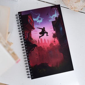 Può includere: Un quaderno a spirale con una copertina rosso scuro e viola che presenta una silhouette di una persona che salta tra gli edifici di una città. La copertina ha un'atmosfera oscura, malinconica e misteriosa.
