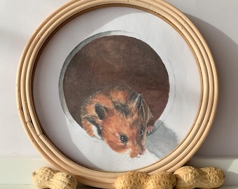 May include: A watercolor painting of a hamster peeking out of a dark brown hole, framed in a round, light brown woven frame. Three peanuts are placed in front of the frame on a white surface.