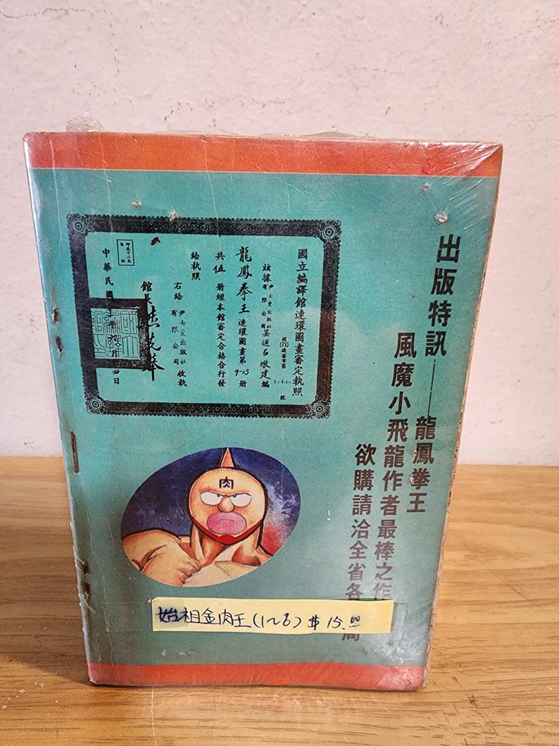 May include: A vintage comic book with a teal cover and orange trim, wrapped in plastic. The cover features Japanese text and an illustration of a muscular character with a red face. The book's title is "Dragon Phoenix Fist King."