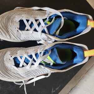 Puede incluir: Un par de zapatillas deportivas blancas y grises con cordones blancos. Las zapatillas tienen un dise&ntilde;o texturizado en los laterales y detalles azules y amarillos en el interior. Adecuadas para correr u otras actividades deportivas.