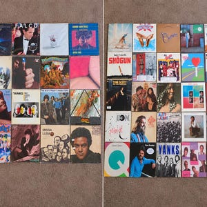 May include: A collection of fifty square vinyl record album covers arranged in two grids. The covers feature diverse graphic designs, photographic portraits, and bold typography, showcasing various musical artists and album titles in a colorful display.