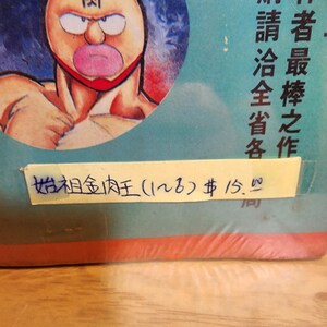 May include: A vintage comic book featuring a muscular cartoon character with a distinctive face, including a large mouth and a red mask. The character is set against a blue background with Japanese text. A yellow sticker displays handwritten text.
