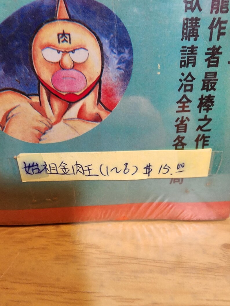 May include: A vintage comic book featuring a muscular cartoon character with a distinctive face, including a large mouth and a red mask. The character is set against a blue background with Japanese text. A yellow sticker displays handwritten text.