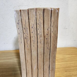 May include: A stack of vintage comic books wrapped in clear plastic. The spines are visible, displaying text and the name "COMICS HOUSE". The books have aged, tan-colored pages and are stacked on a wooden surface.