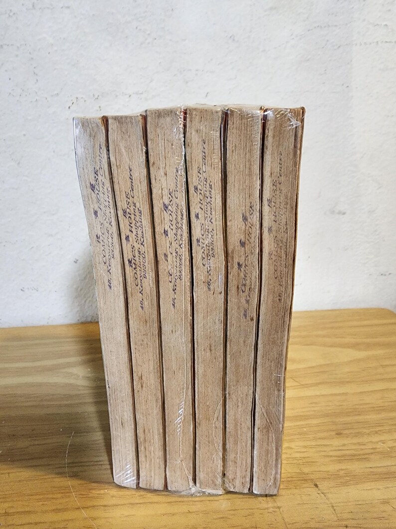 May include: A stack of vintage comic books wrapped in clear plastic. The spines are visible, displaying text and the name "COMICS HOUSE". The books have aged, tan-colored pages and are stacked on a wooden surface.