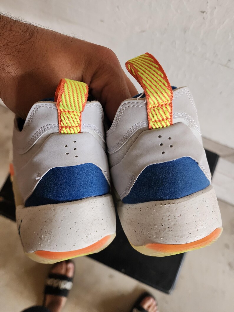 Puede incluir: Par de zapatillas blancas y azules con detalles en naranja y amarillo. Las zapatillas tienen una entresuela moteada y una leng&uuml;eta en el tal&oacute;n. Las suelas son naranjas.