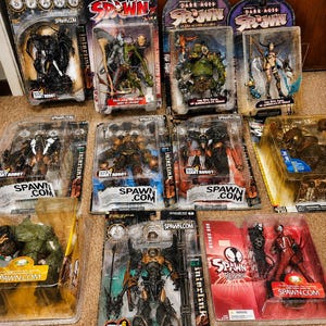 Könnte beinhalten: Eine Sammlung von elf Spawn-Actionfiguren in ihrer originalen Kunststoff-Blisterverpackung. Die Figuren zeigen verschiedene Charaktere, darunter Roboter, Krieger und Kreaturen, mit sichtbarem Branding wie Spawn.com und Dark Ages.