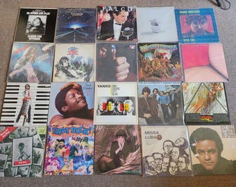 May include: A selection of vinyl record albums with a variety of cover art. The covers showcase portraits, landscapes, and abstract designs. Some covers display text such as "FALCO", "YANKS ONLY LOVERS LEFT ALIVE", and "FRAT ROCK!".