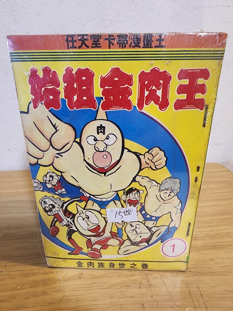 May include: A vintage Japanese comic book titled "Kinnikuman" (Muscle Man) in a yellow, red, and blue color scheme. The cover features a muscular cartoon character with a fist raised, surrounded by other characters. The text on the cover is in Japanese.
