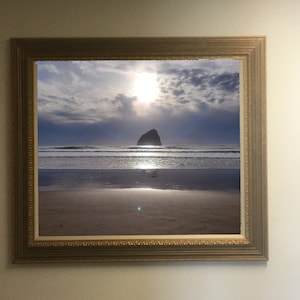 Könnte beinhalten: Ein gerahmtes Foto einer felsigen Insel im Meer mit einem Sandstrand im Vordergrund. Die Sonne scheint hell am Himmel und es gibt Wolken am Himmel.