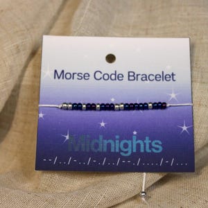 May include: A white string bracelet with blue and silver beads. The bracelet is on a card that says "Morse Code Bracelet" and "Midnights".