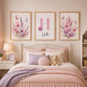 May include: Three framed wall art prints featuring floral arrangements with pink and purple flowers and butterflies. The center print displays a large pink letter H above the name Halle in black script. The prints are in light wood frames.