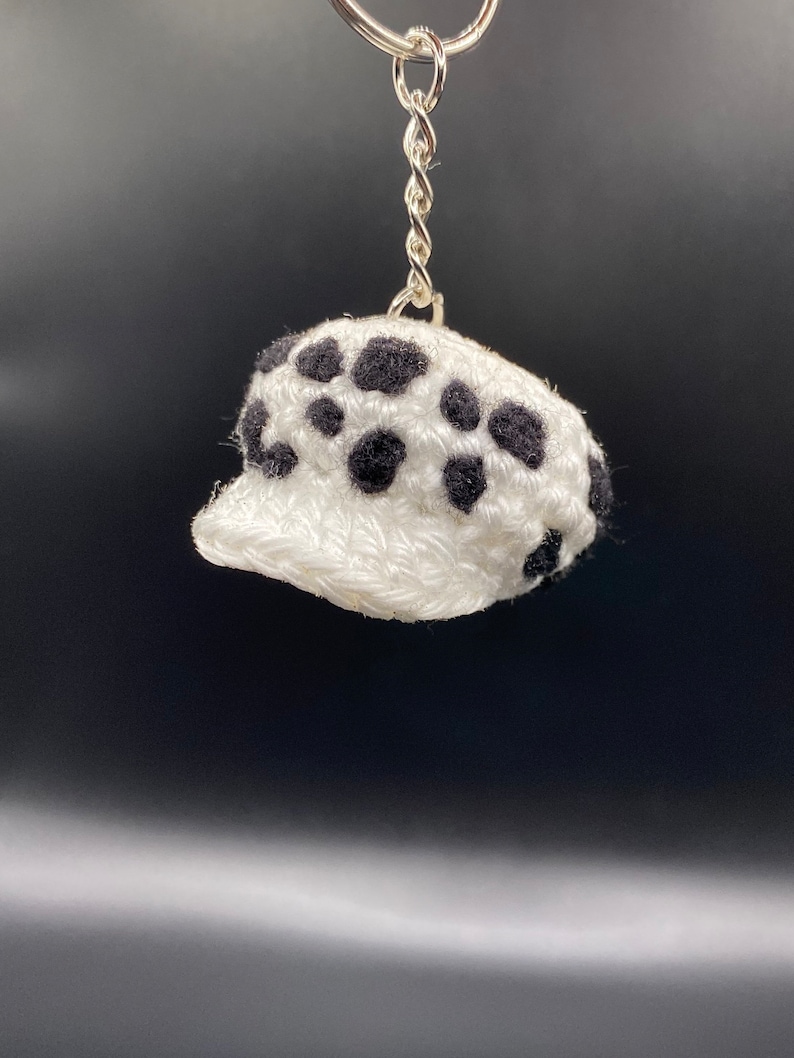 May include: White crocheted hat with black polka dots, attached to a silver keychain.