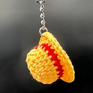 May include: A yellow crocheted hat with red stripes attached to a silver keychain.