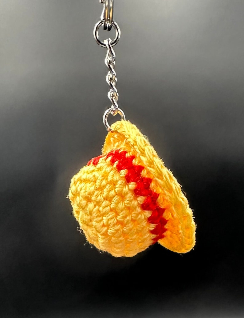 May include: A yellow crocheted hat with red stripes attached to a silver keychain.