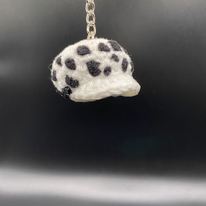 May include: White crocheted hat with black spots, shaped like a baseball cap, attached to a silver keychain.