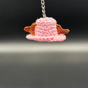 May include: A pink crocheted hat with brown crocheted accents, attached to a silver keychain.