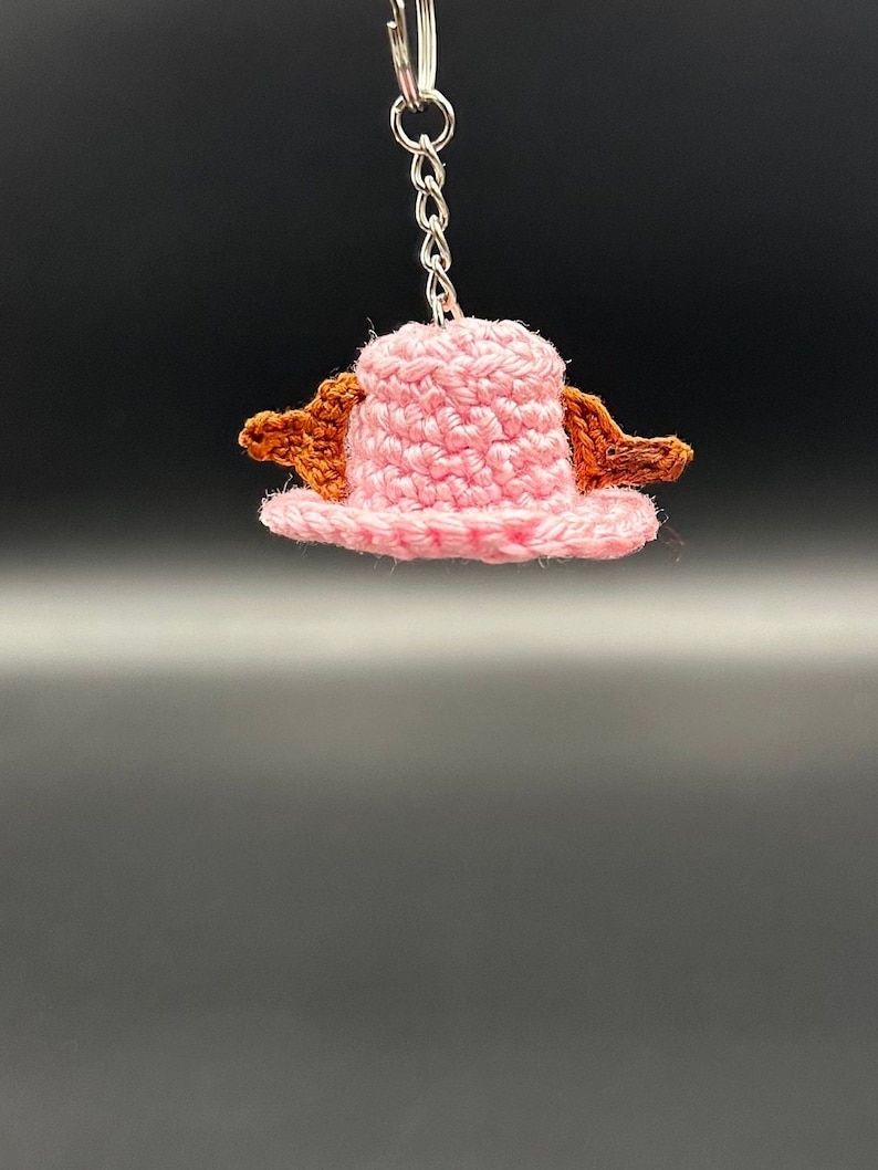 May include: A pink crocheted hat with brown crocheted accents, attached to a silver keychain.