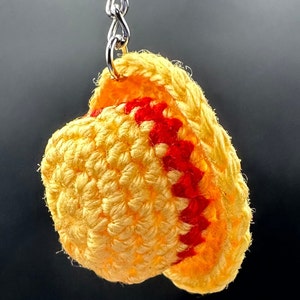 May include: A crocheted yellow and red hat keychain. The hat is made of yarn and has a red trim.