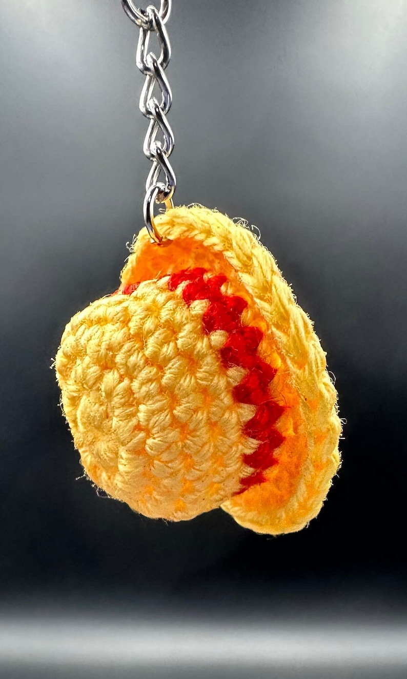May include: A crocheted yellow and red hat keychain. The hat is made of yarn and has a red trim.