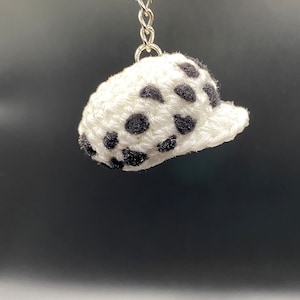 May include: A white crocheted hat with black polka dots attached to a silver keychain.