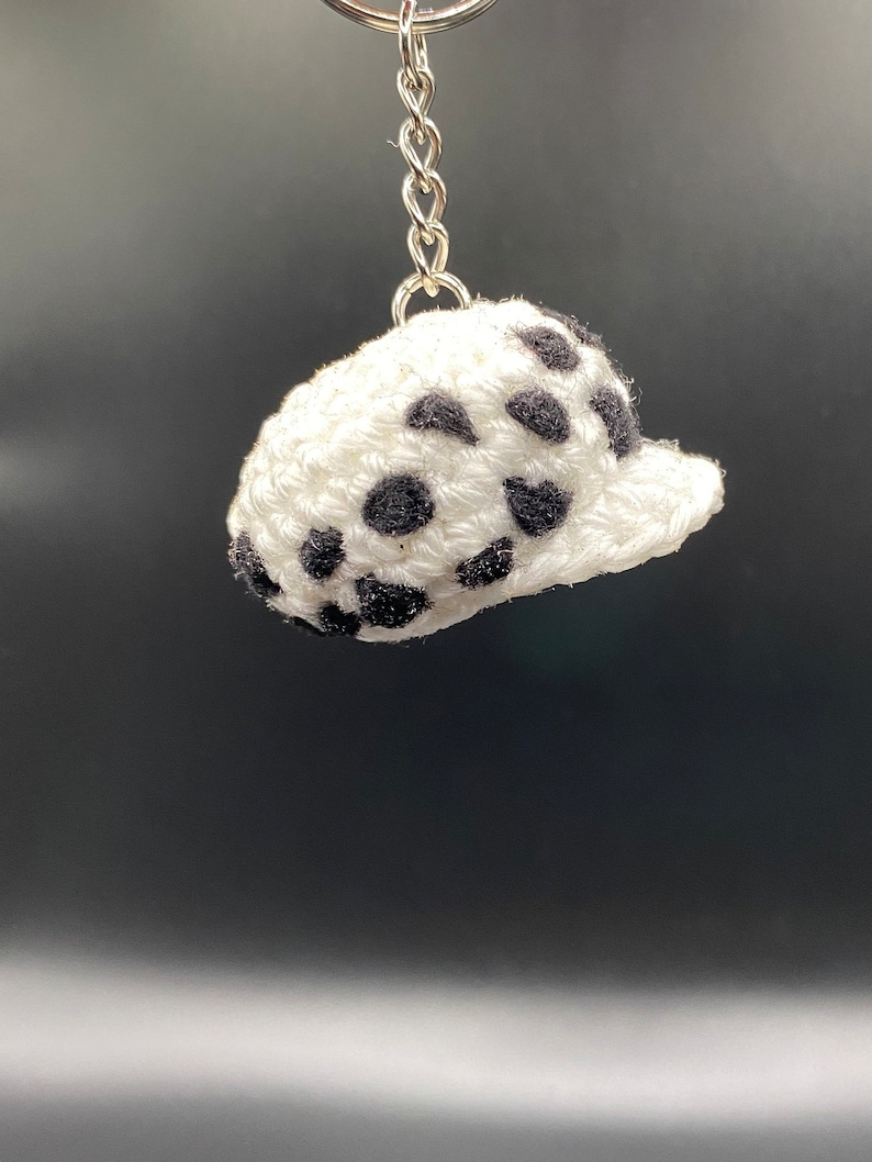 May include: A white crocheted hat with black polka dots attached to a silver keychain.
