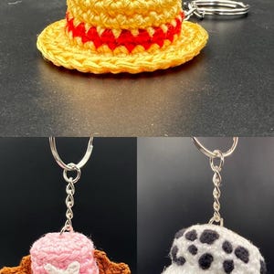 May include: Three crocheted hats with keychains. The first hat is yellow with a red band, the second is pink with brown accents and a white cross, and the third is white with black spots.