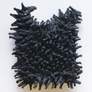 May include: A black textile sculpture made of many small, folded pieces of fabric. The sculpture is shaped like a large, irregular blob.