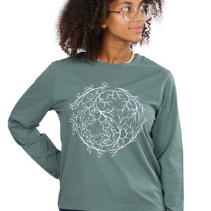 A woman with curly hair wearing a green long-sleeved shirt with a white leaf design on it.