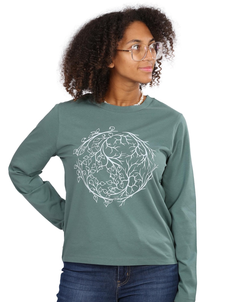 A woman with curly hair wearing a green long-sleeved shirt with a white leaf design on it.
