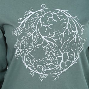 A close-up image of a person wearing a green t-shirt with a white circular design featuring a tree-like pattern.